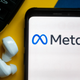 The Meta logo displayed on a smartphone next to wireless earphones and... car keys, for some reason. Used here as stock photo.